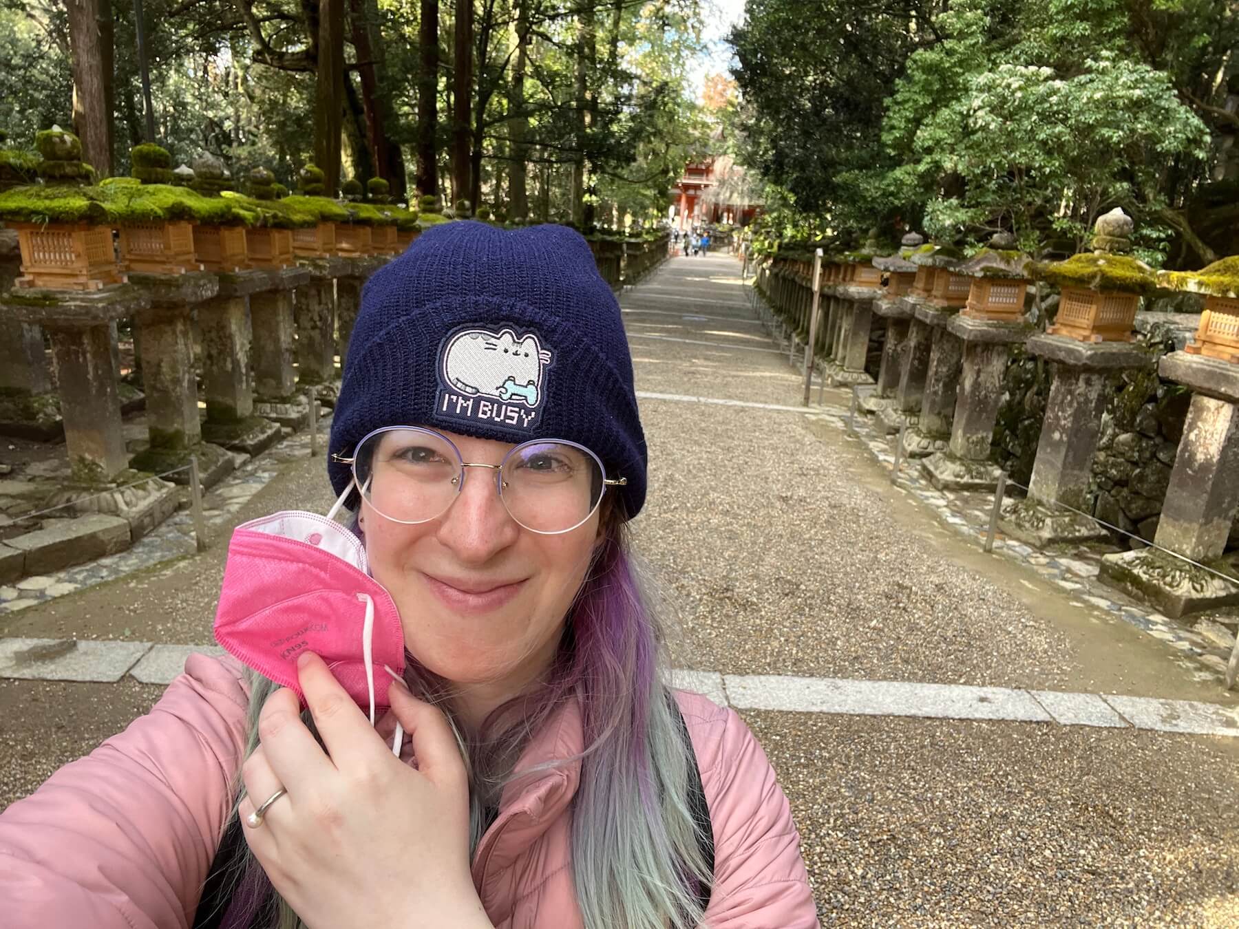 A woman walking in the park wearing a beanie and taking off a mask